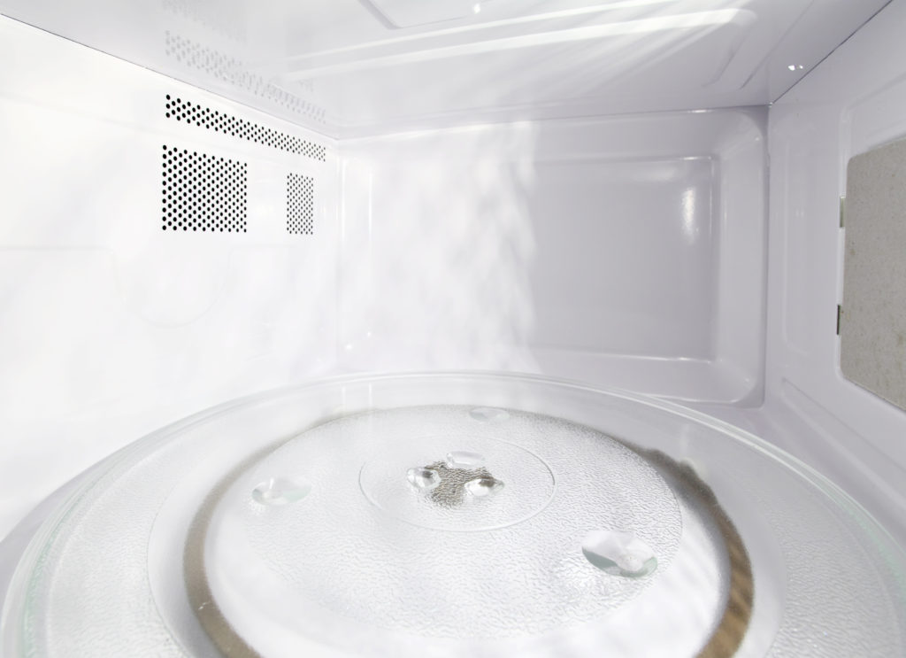Interior de um micro-ondas limpo e vazio, com prato giratório de vidro e gotas de água sobre a superfície.