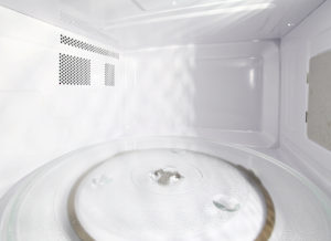 Interior de um micro-ondas limpo e vazio, com prato giratório de vidro e gotas de água sobre a superfície.